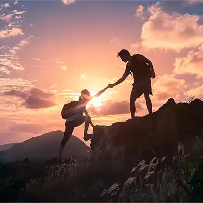 Someone helping another climb a mountain.